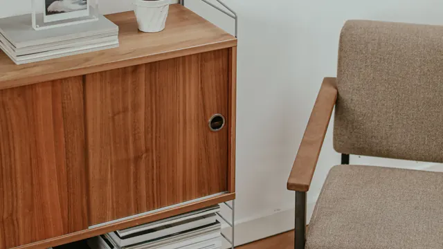 Wooden sliding-door cabinet beside an upholstered armchair, with magazines on a lower shelf