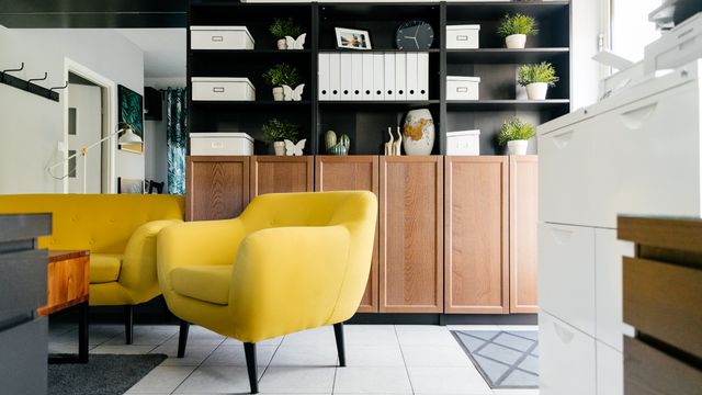 A yellow armchair in front of a shelving unit with open shelves, storage boxes and cupboards