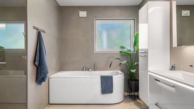 Contemporary bathroom with a white bathtub, frosted window, extractor fan vent in the wall, and tall storage cabinet.