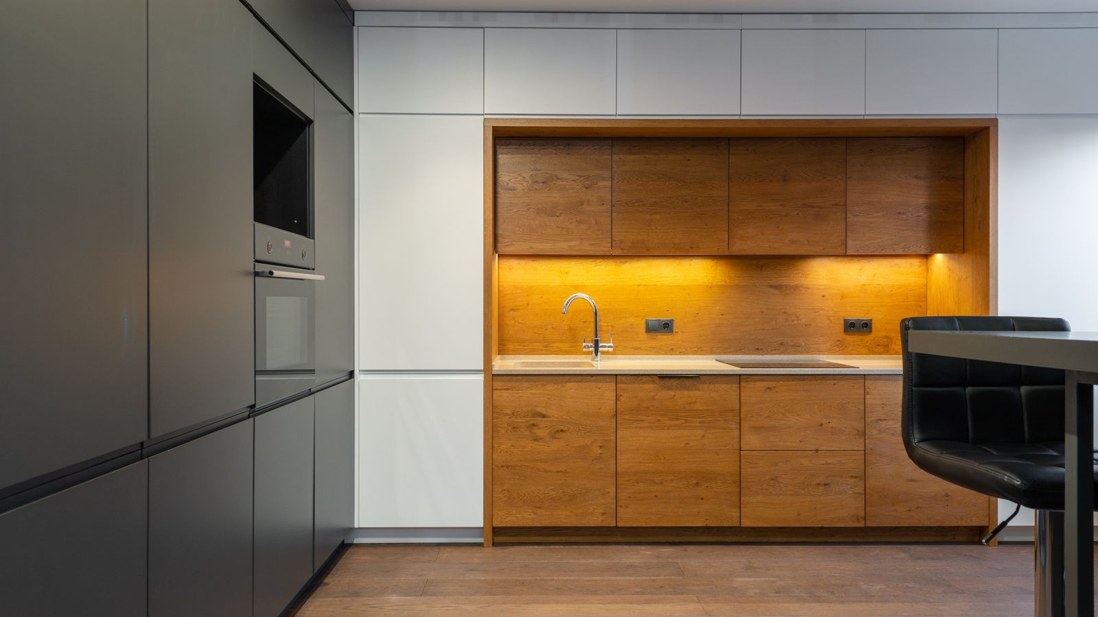 Contemporary kitchen fitted with wood-effect cabinets, warm under-cabinet lighting, integrated appliances, and grey cabinetry.