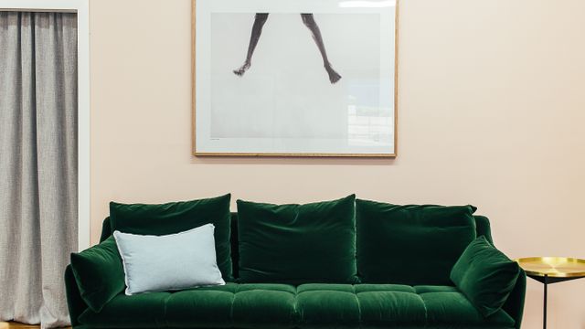 A green velvet three-seater sofa with scatter cushions against a neutral wall.