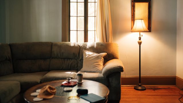 A lit shaded floor lamp standing next to a sofa and coffee table in a living room.