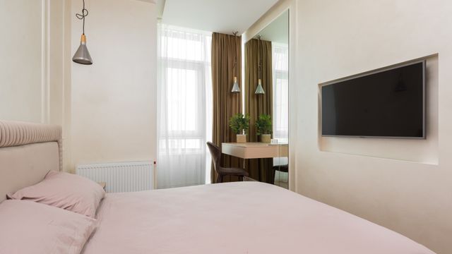 Compact modern bedroom featuring a neatly made bed with soft pink linen, pendant lighting, and a slim dressing table by the window.