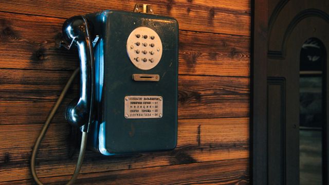 A vintage wall-mounted pay telephone fixed to a dark wood-panelled wall.