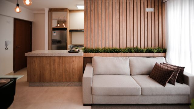Modern living room interior with a beige sofa against a vertical slatted timber wall partition beside an open kitchen counter.