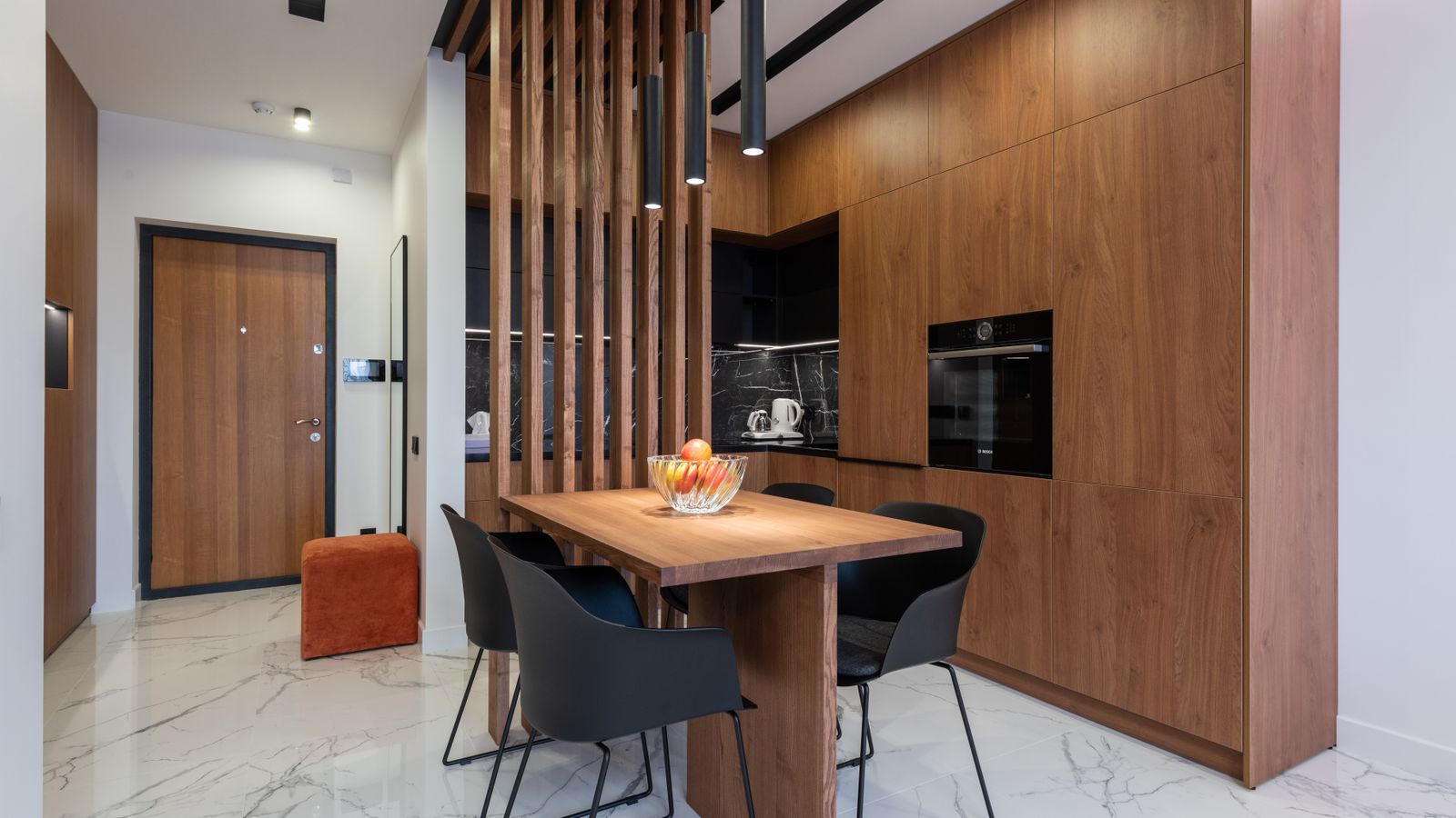 Modern open-plan kitchen and dining area with tall timber cabinetry, wooden slatted partition screen and dining table with chairs.