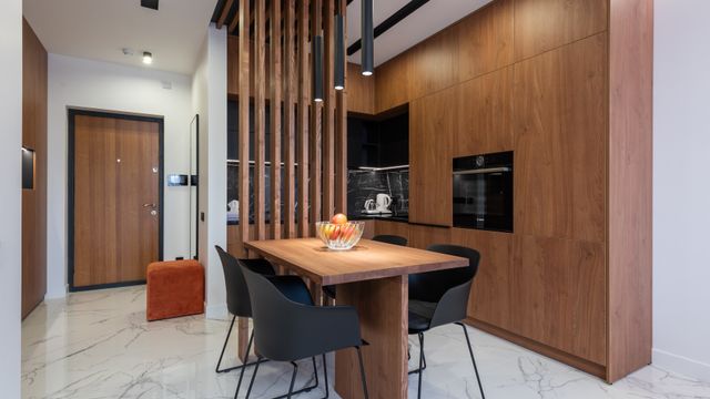 Modern open-plan kitchen and dining area with tall timber cabinetry, wooden slatted partition screen and dining table with chairs.