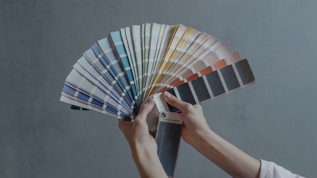 Hands holding an open fan deck of colour paint swatches against a grey background